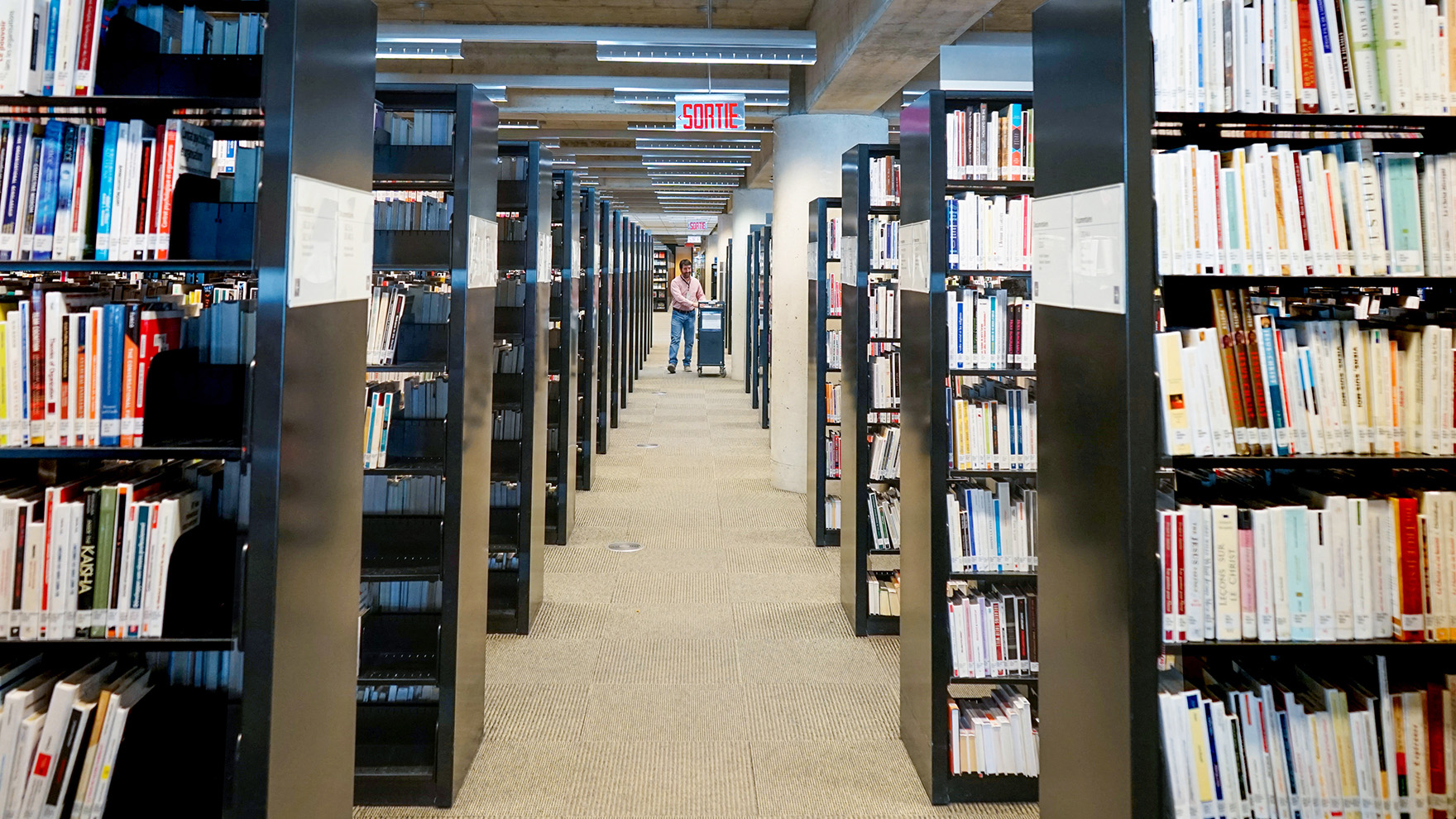 Rayonnages de livres à la Grande Bibliothèque. Membre du personnel avec un chariot de livres.