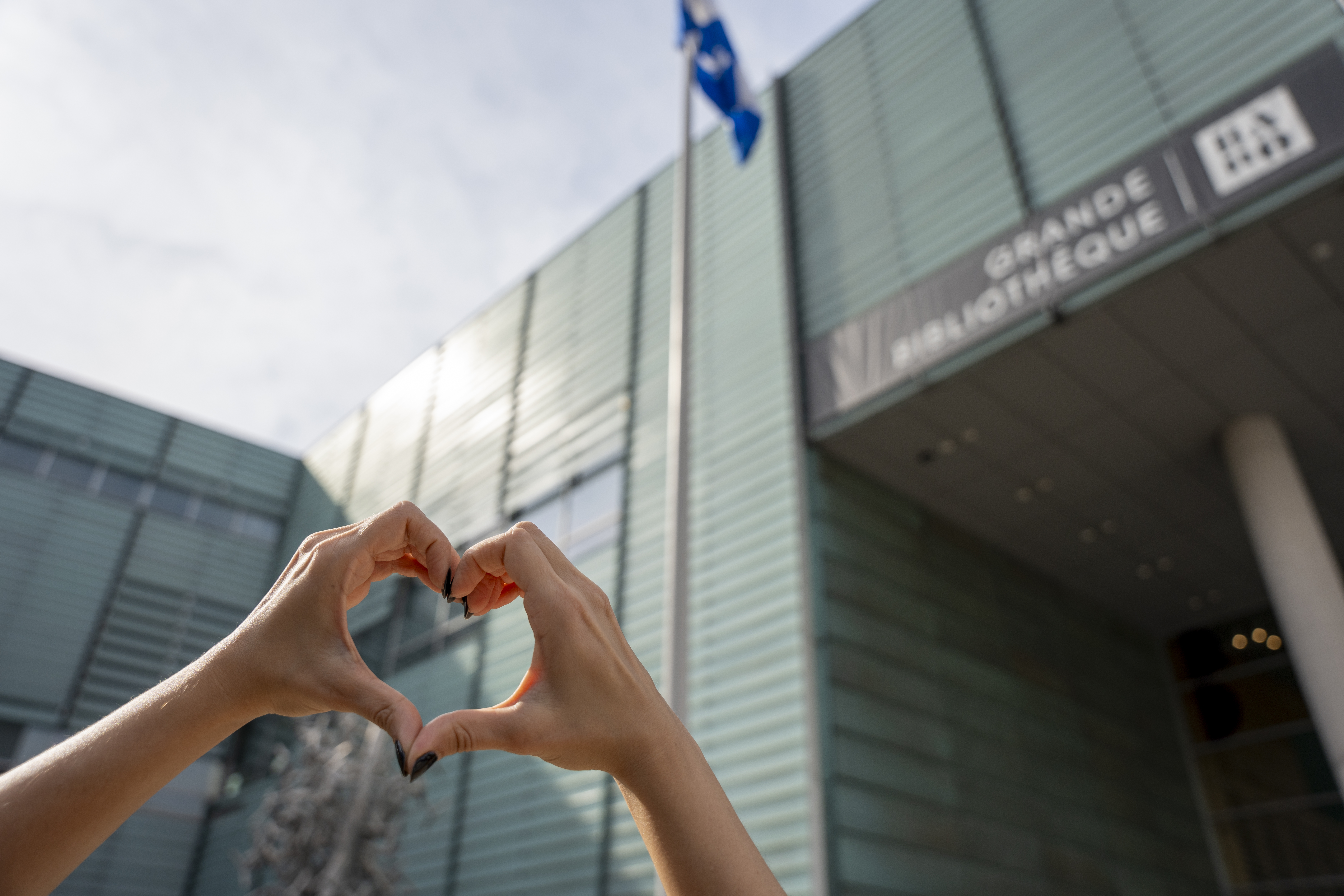 Quelqu'un forme un coeur avec ses mains devant la façade de la Grande Bibliothèque.