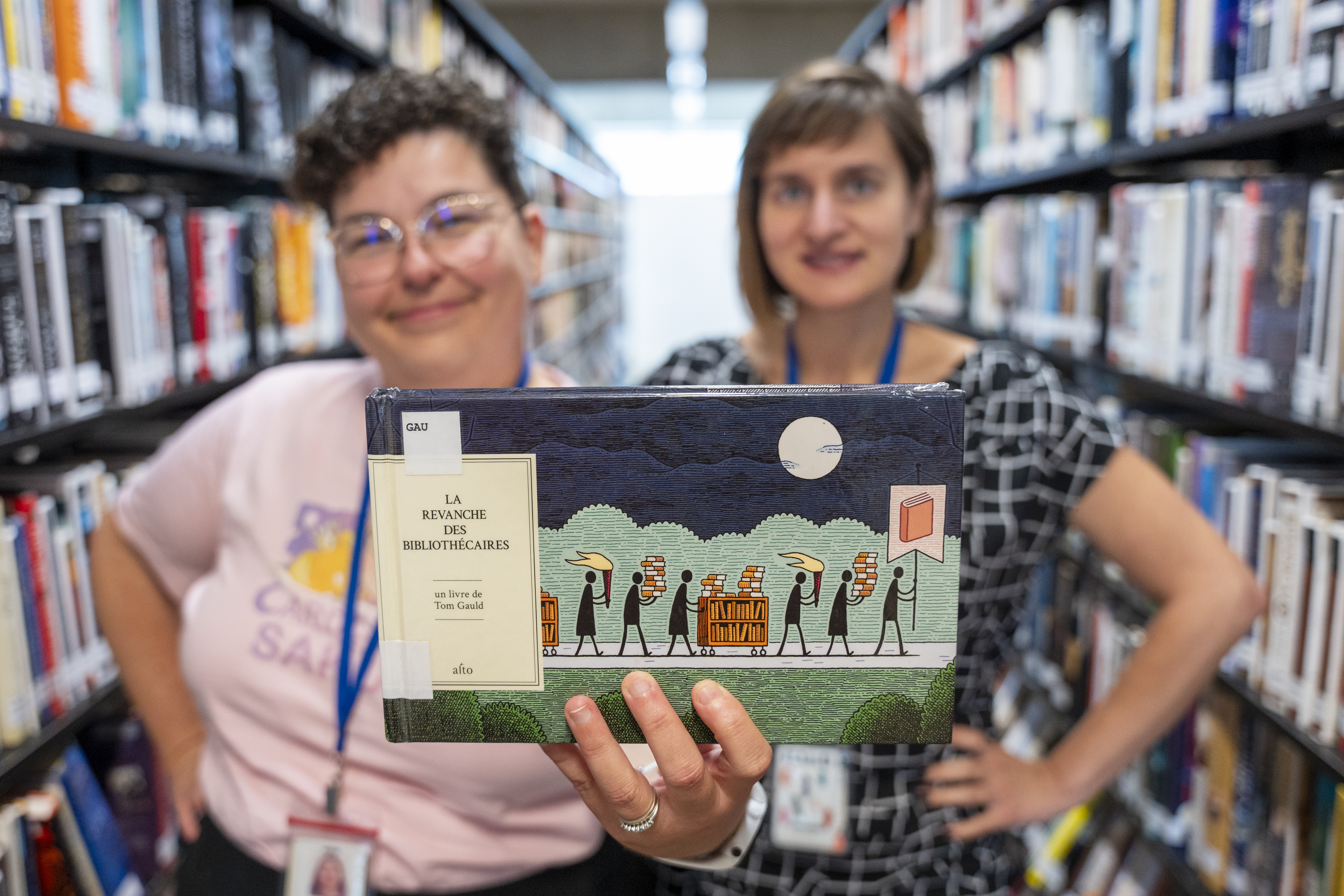 Deux femmes, dans une bibliothèque, montrent la bande dessinée « La revanche des bibliothécaires ».
