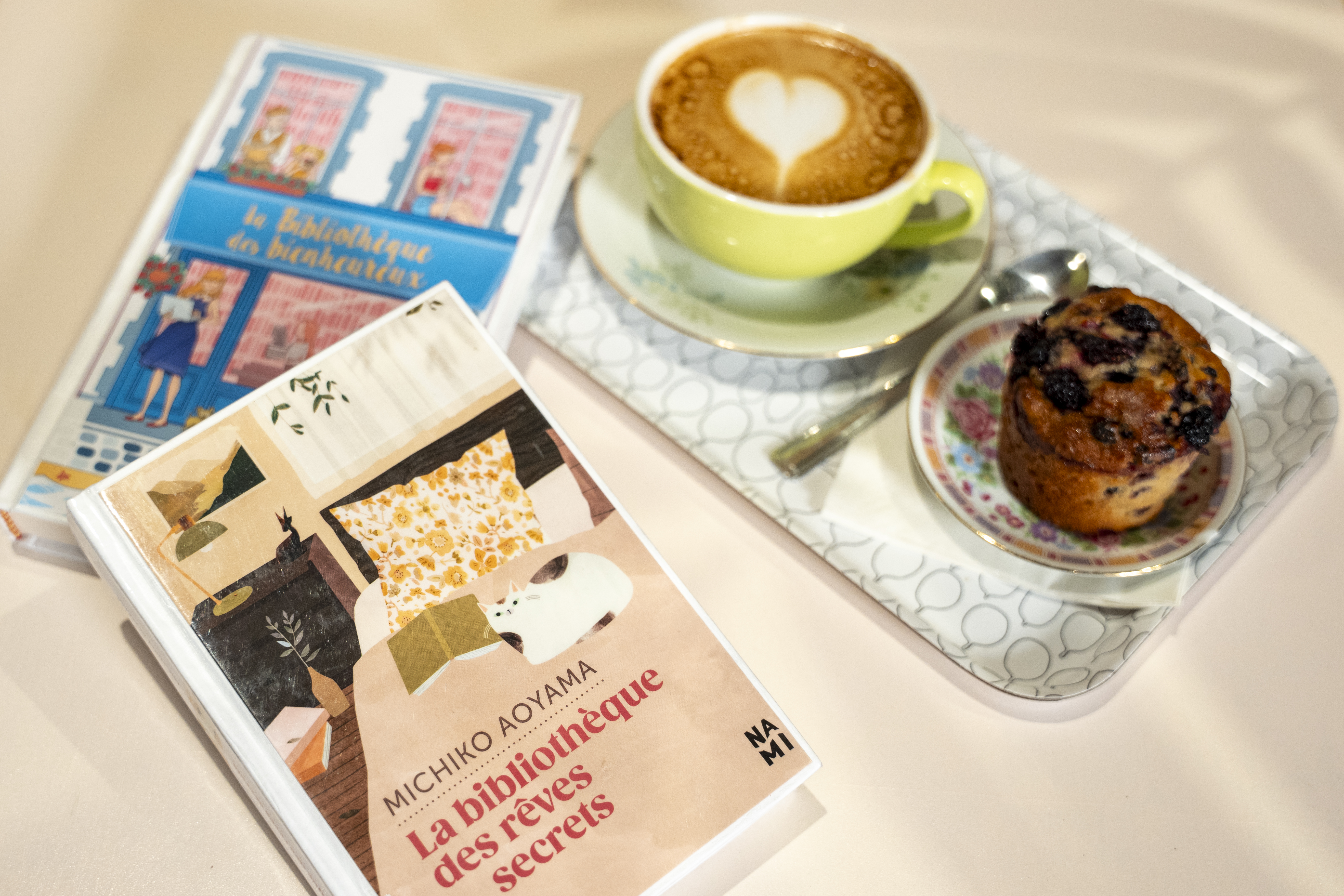 À côté d'une tasse de café et d'un muffin, deux livres : « La bibliothèque des bienheureux » et « La bibliothèque des rêves secrets ».
