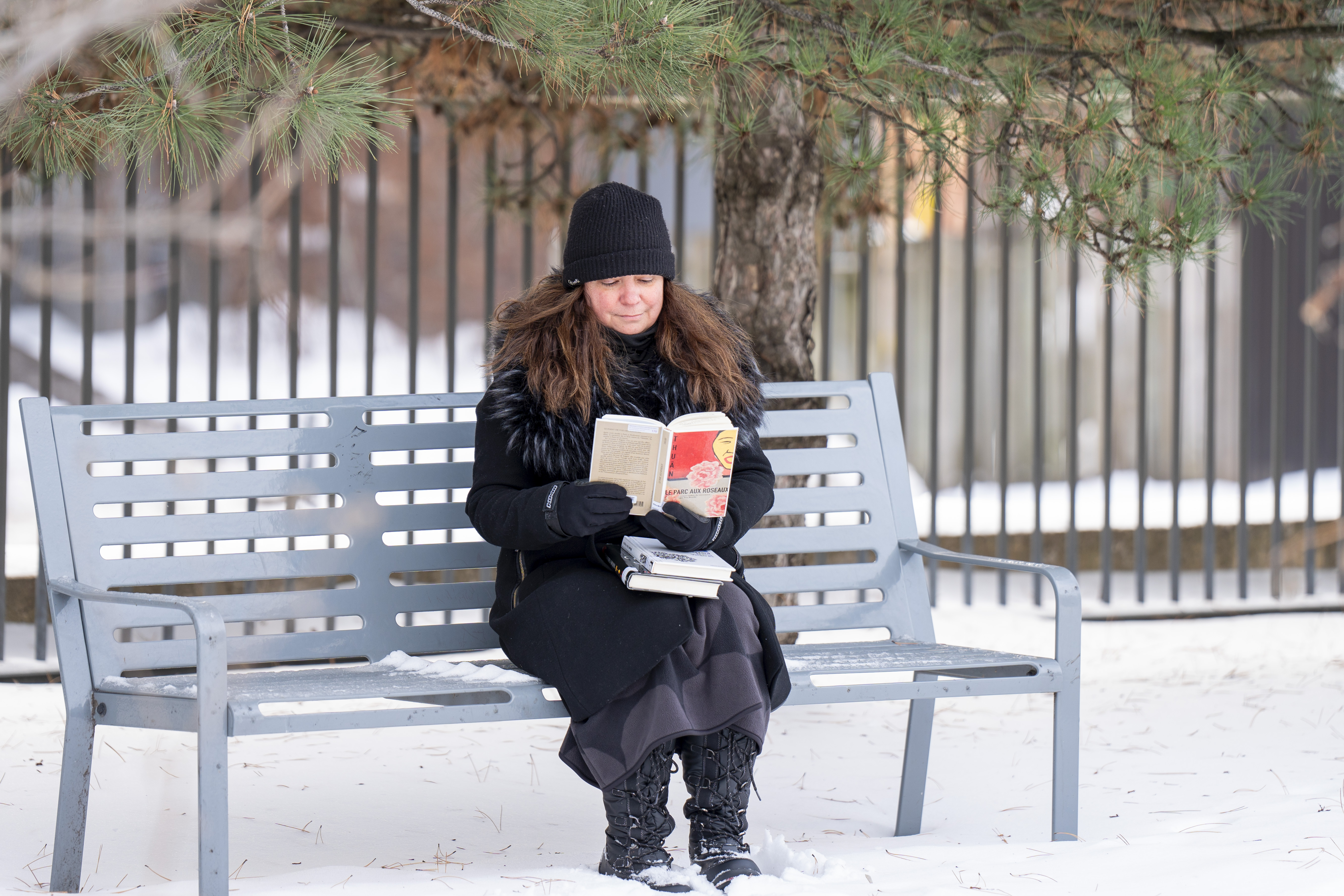 Une femme lit un livre sur un banc dans la neige.