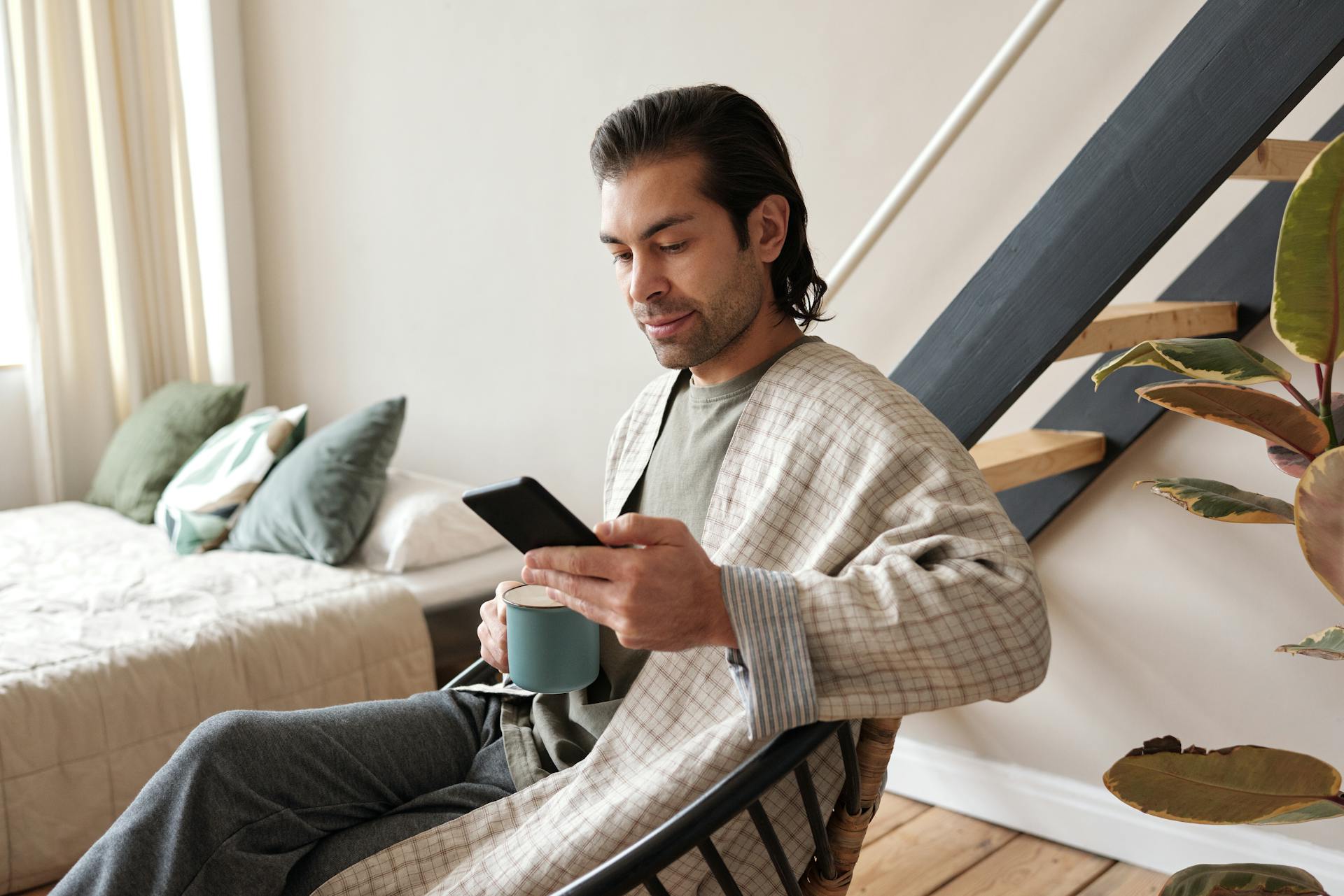 Photo d'un homme assis regardant son cellulaire et tenant un café