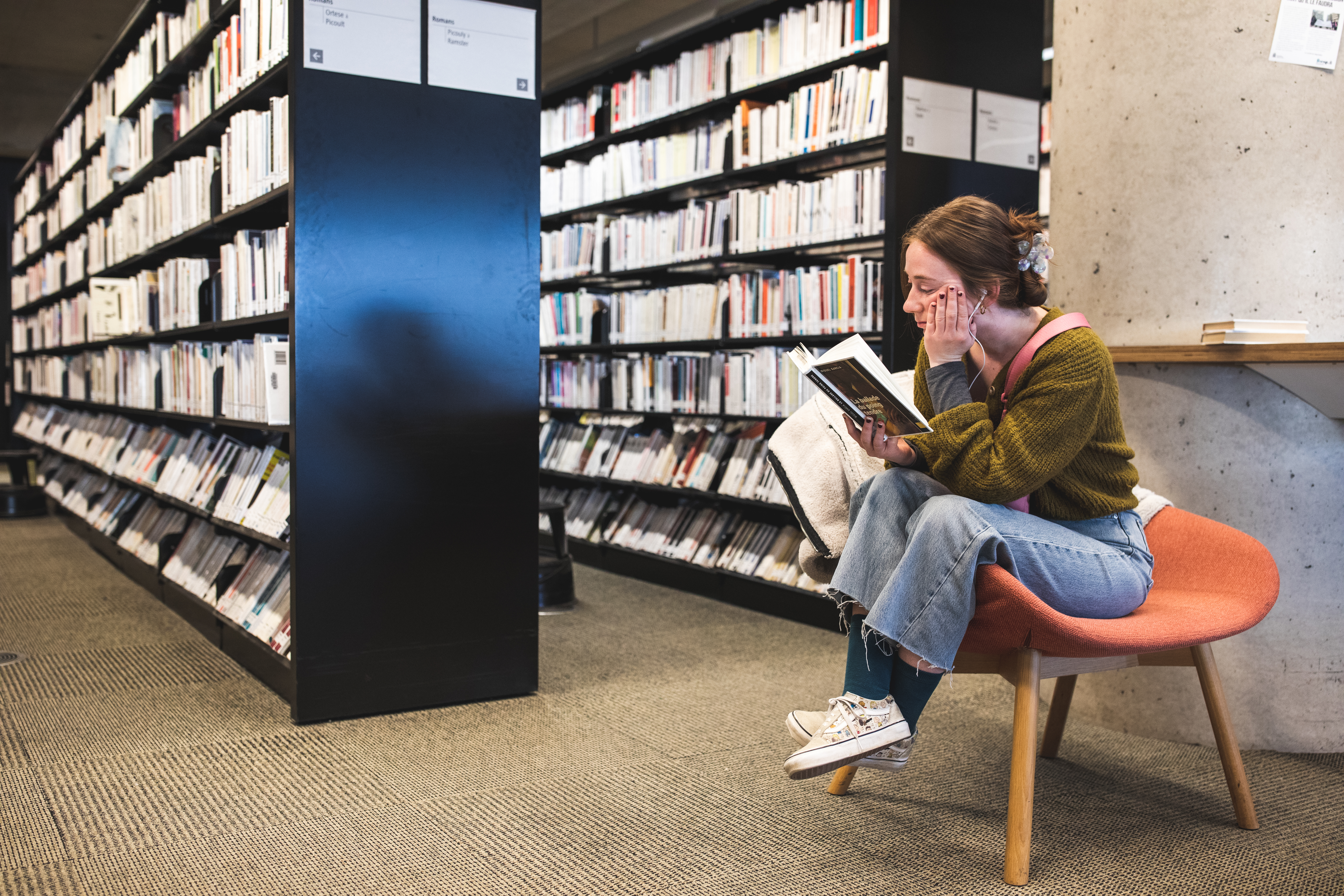 Jeune femme lisant un livre près de rayonnages