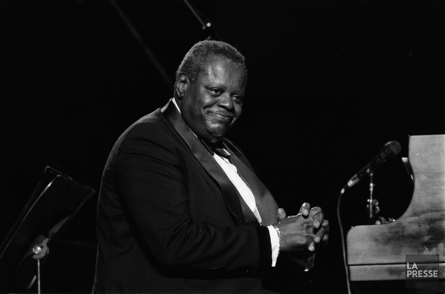 Oscar Peterson, assis au piano, sourit au public.