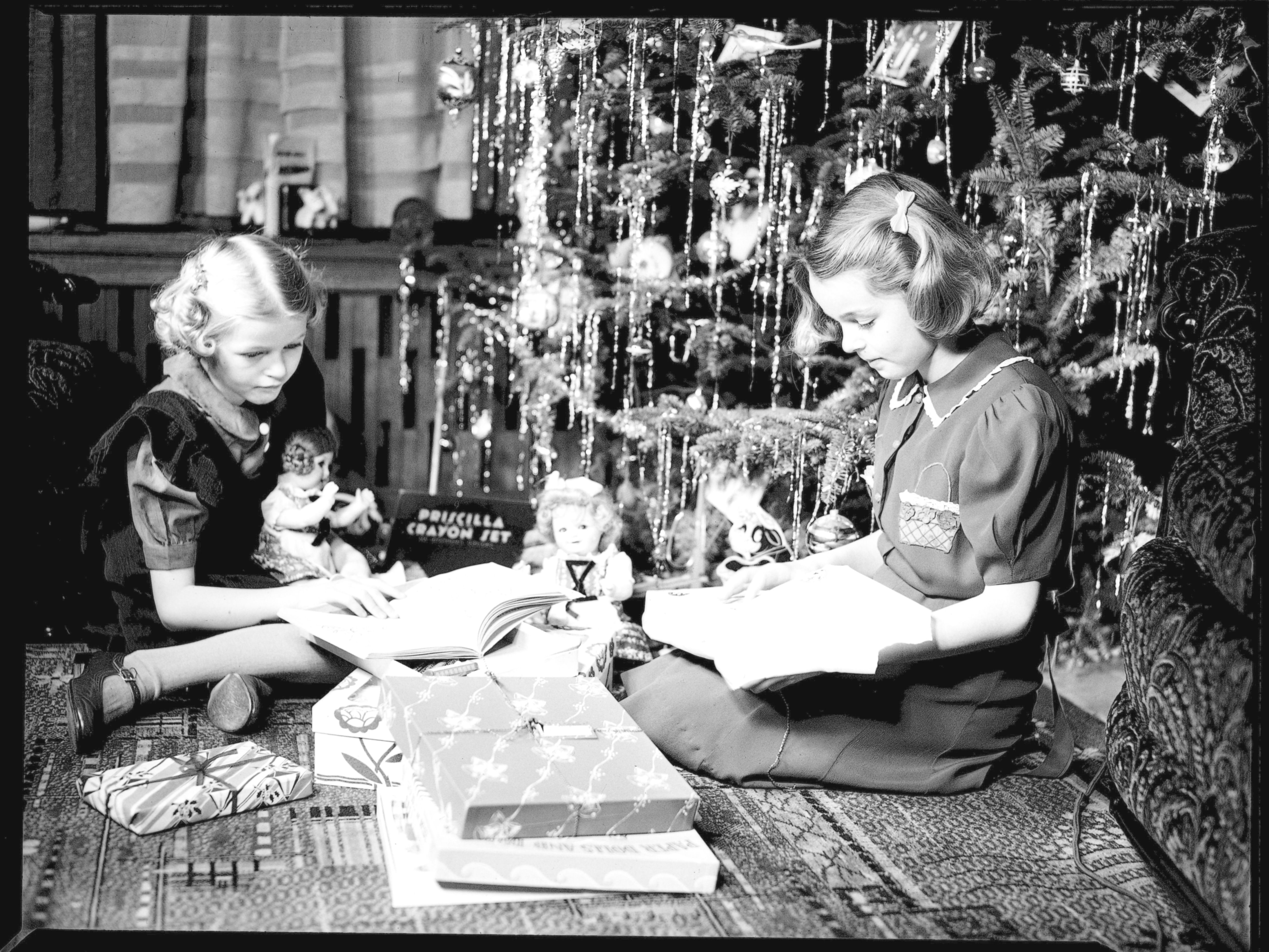 Deux fillettes jouent avec leurs cadeaux au pied d’un arbre de Noël.
