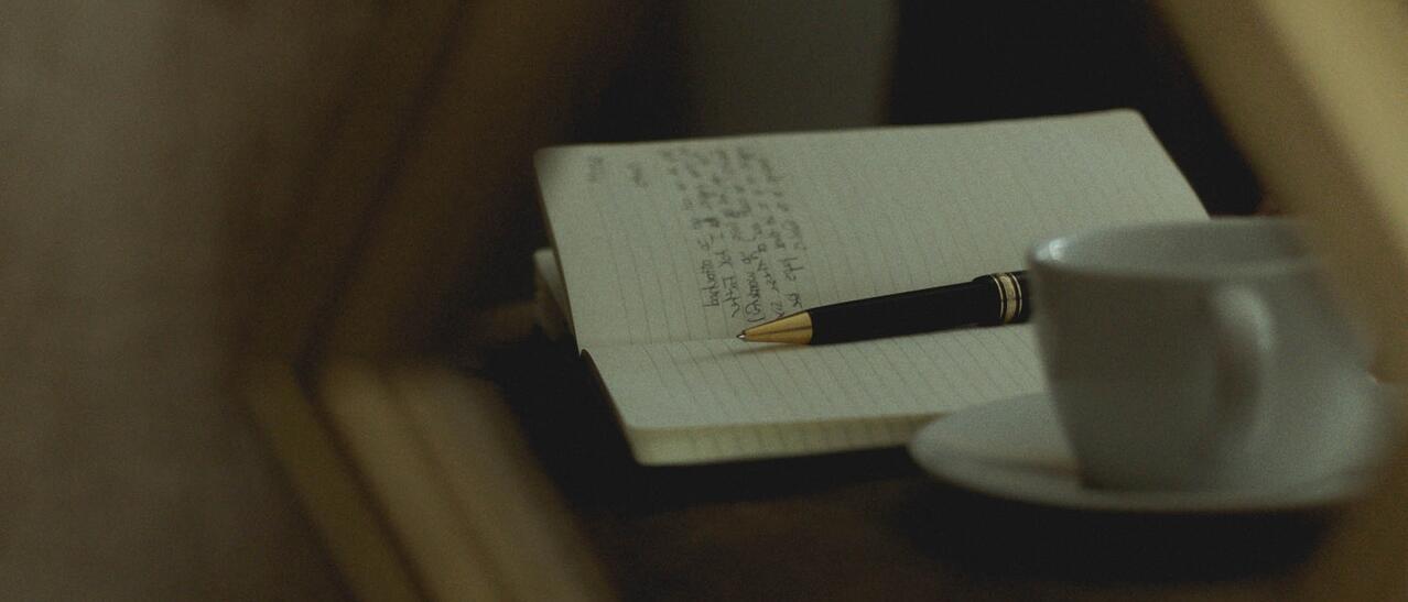 Reflet dans un miroir d'une cahier, d'un stylo et d'une tasse à café.