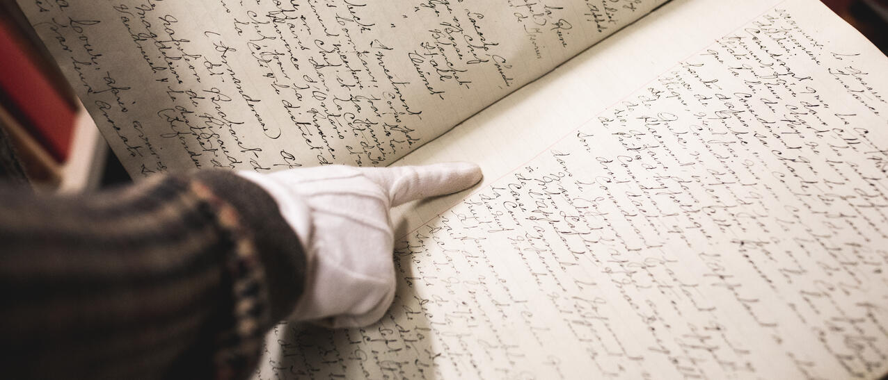 Une main pointe un texte dans un registre manuscrit