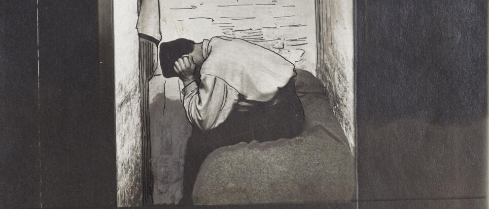 Un homme pose la tête sur ses genoux, assis sur un lit dans une cellule de prison. 