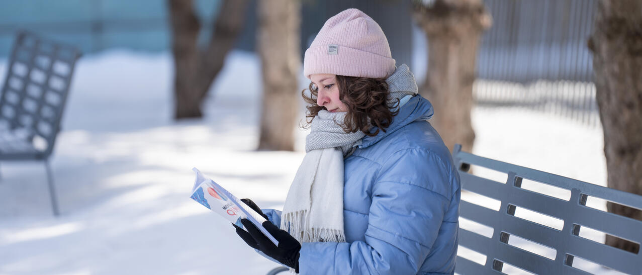 Une femme lit un livre sur un banc dans la neige.