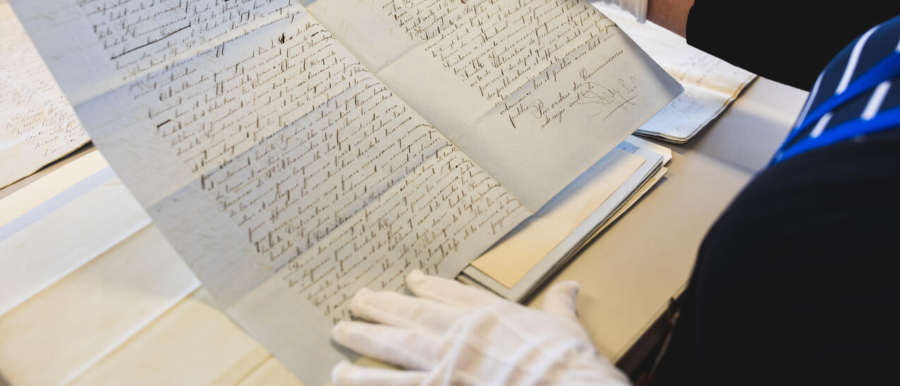 Une personne tient un document d'archives avec des gants blancs.