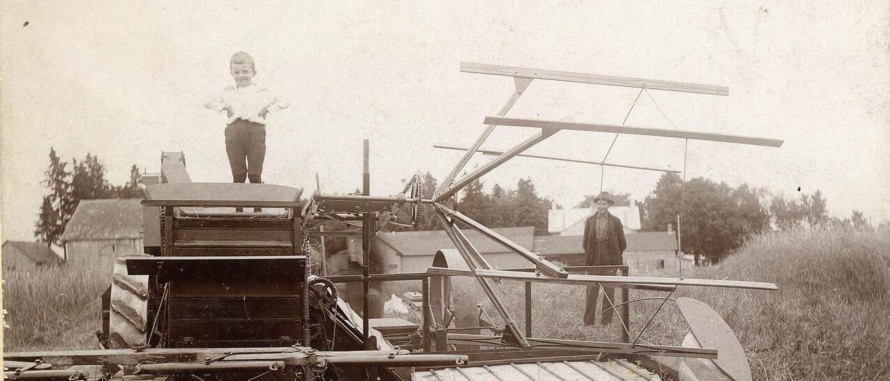 Photo noir et blanc d'un enfant et d'un homme posant près d'une machine agricole.