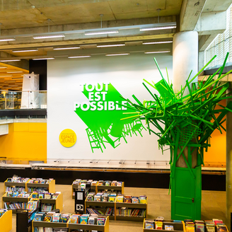Rayons de livres jouxtant une installation d'art faite de matériaux recyclés, intitulée « Tout est possible ».
